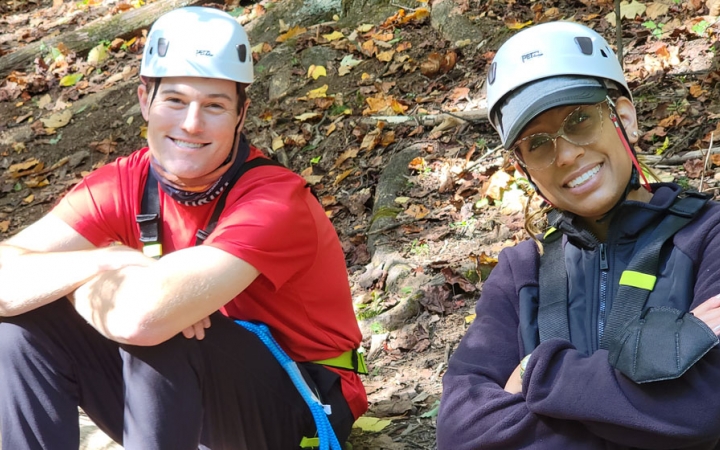 two people wearing helmets smile at the camera